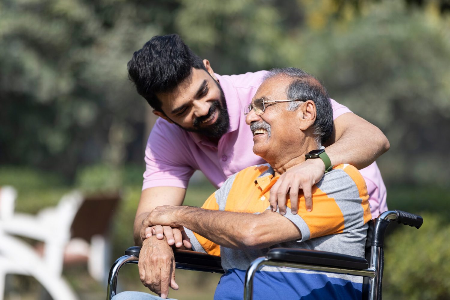 A caregiver embracing an elderly man in a wheelchair outdoors